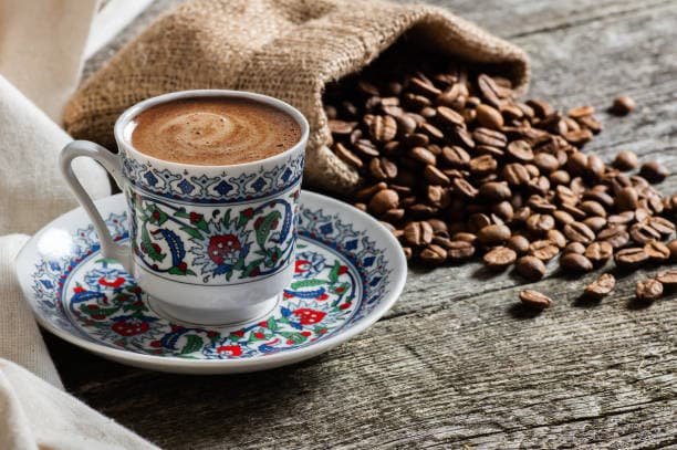 An ornate Turkish coffee cup beside a sack of coffee beans